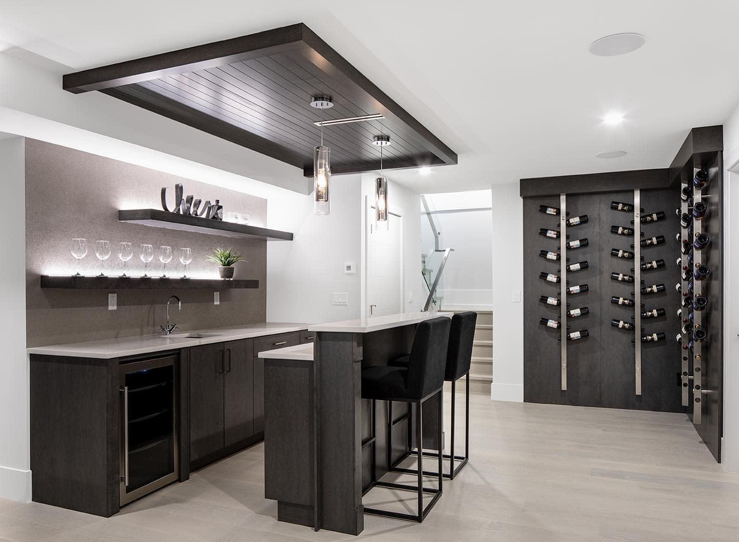 Modern basement kitchen with wine rack, sleek bar seating, and illuminated shelving.